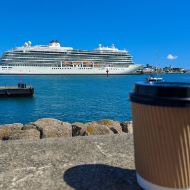 A cup of coffee on a ledge with a view of a cruise ship in the distance.