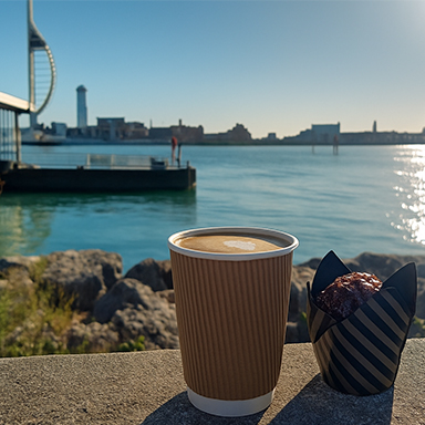 A cup of coffee beside a muffin resting on a ledge, with soft natural light illuminating the scene.