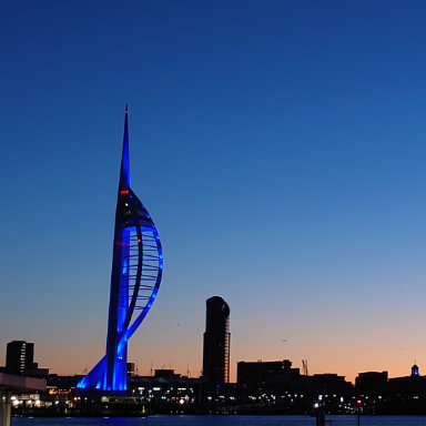Spinnaker Tower illuminated in blue at dusk, standing tall against a twilight sky.