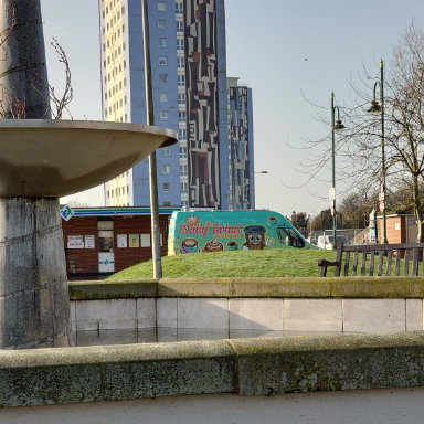 The Daily Grind coffee van parked in the background behind a fountain and in front of a tall building.